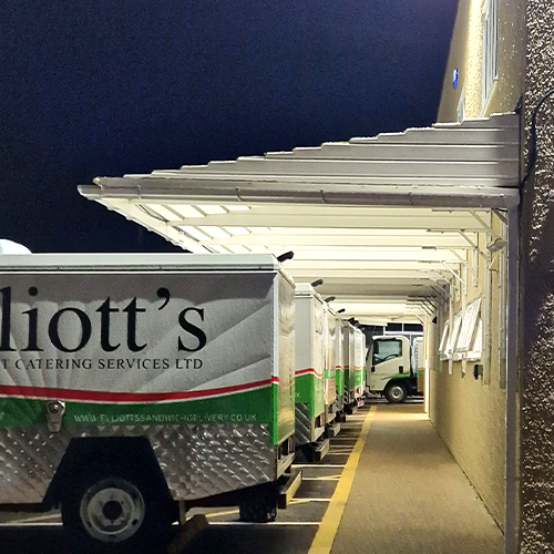 A white loading bay canopy attached to a building with several vans branded in the Elliott's upper crust catering serives logo.