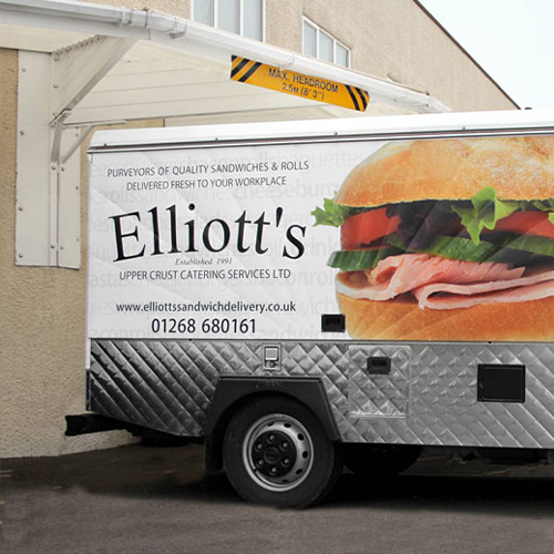 A white and silver van branded in the Elliott's upper crust catering services logo. The van is under a white loading bay canopy